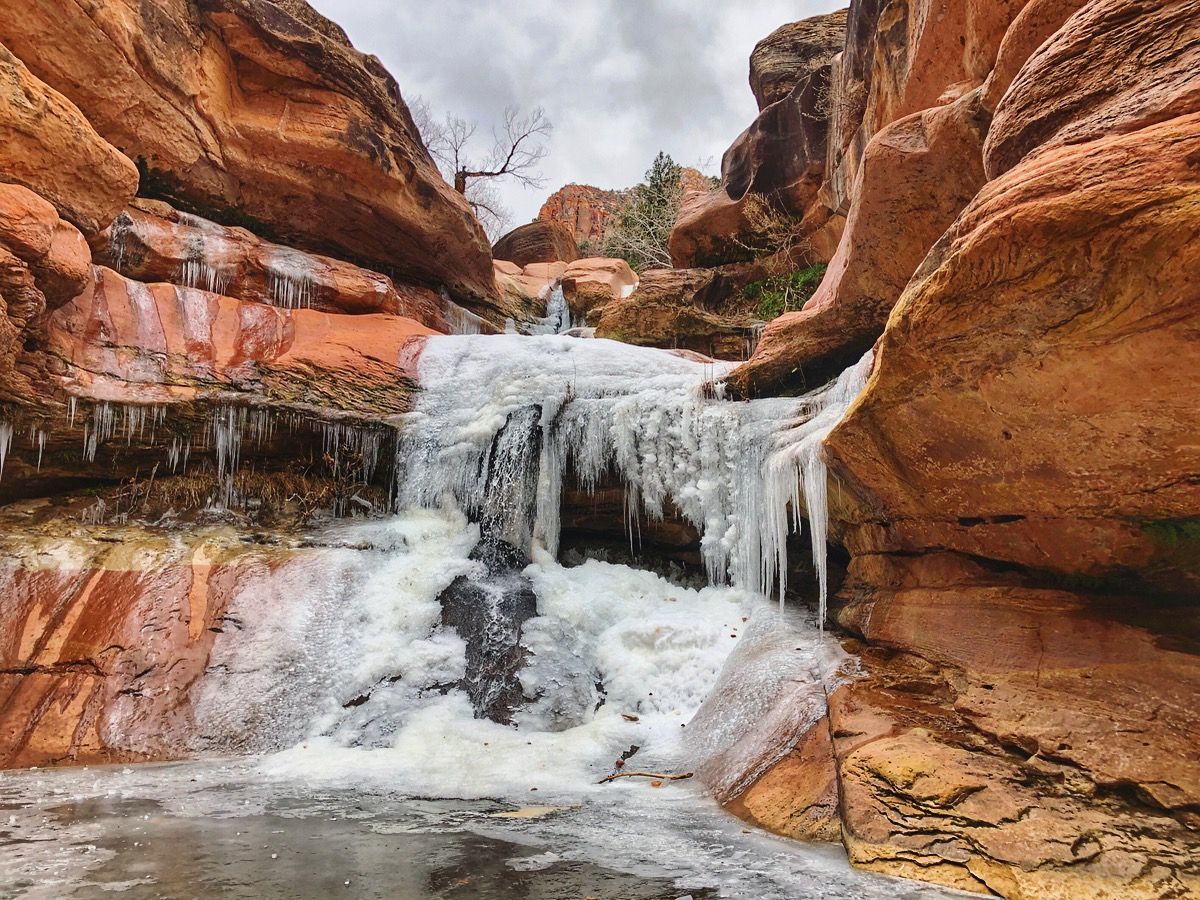 Frozen waterfall cascading over red rock cliffs.