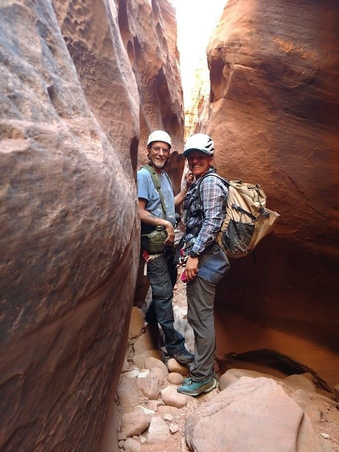 Two people wearing helmets and harnesses stand in a narrow slot canyon.