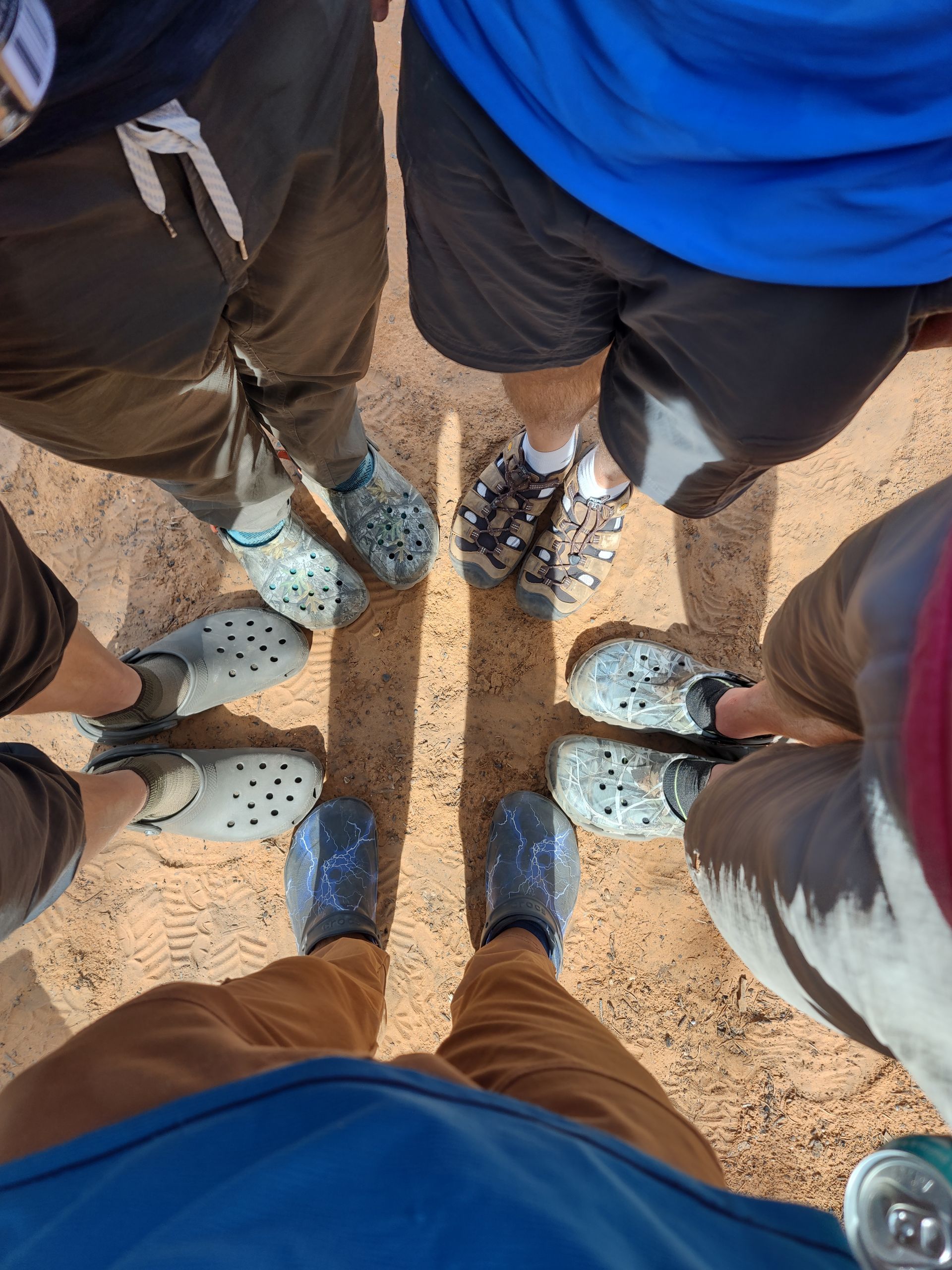 People standing in a circle, showing their shoes on sandy ground.