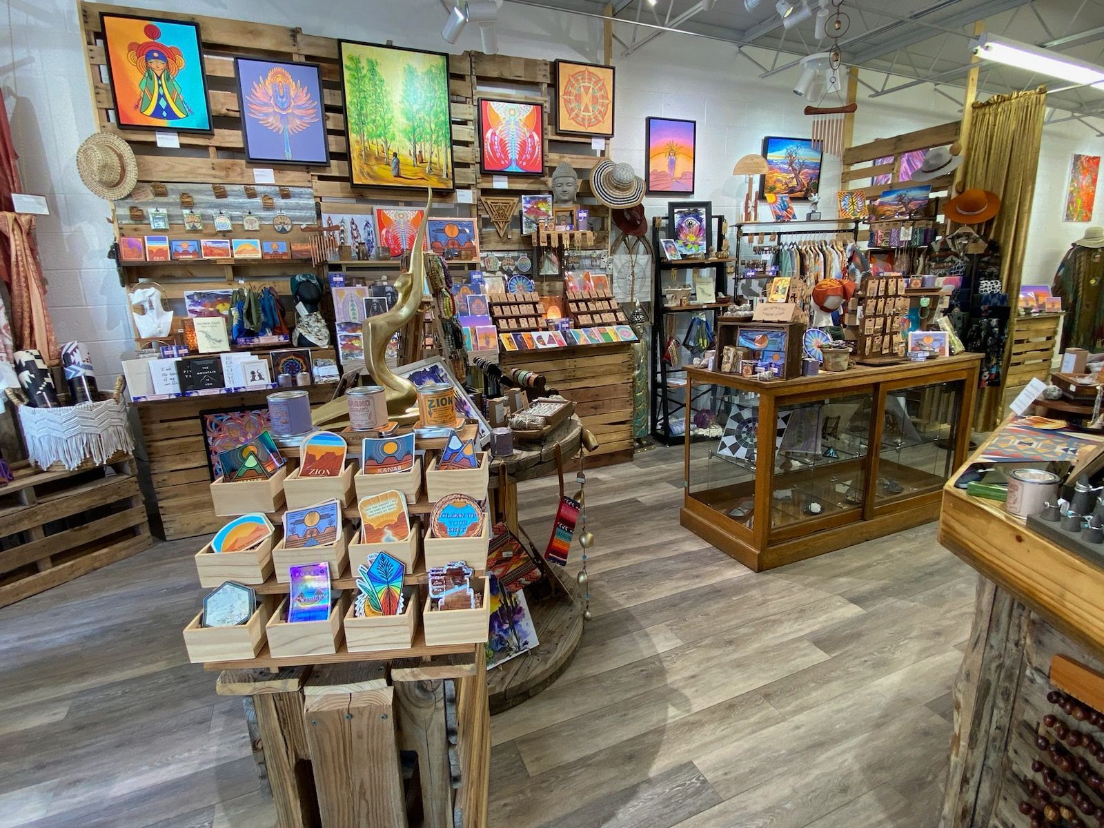 A brightly lit art gallery with wooden floors and walls. Artwork, jewelry, and cards are displayed for sale.