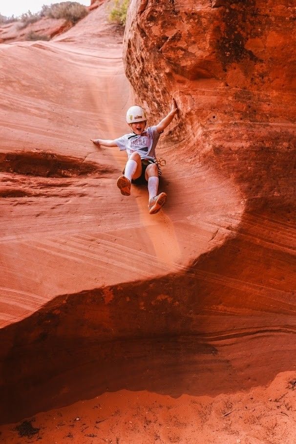 A young boy is sliding down a rock wall.