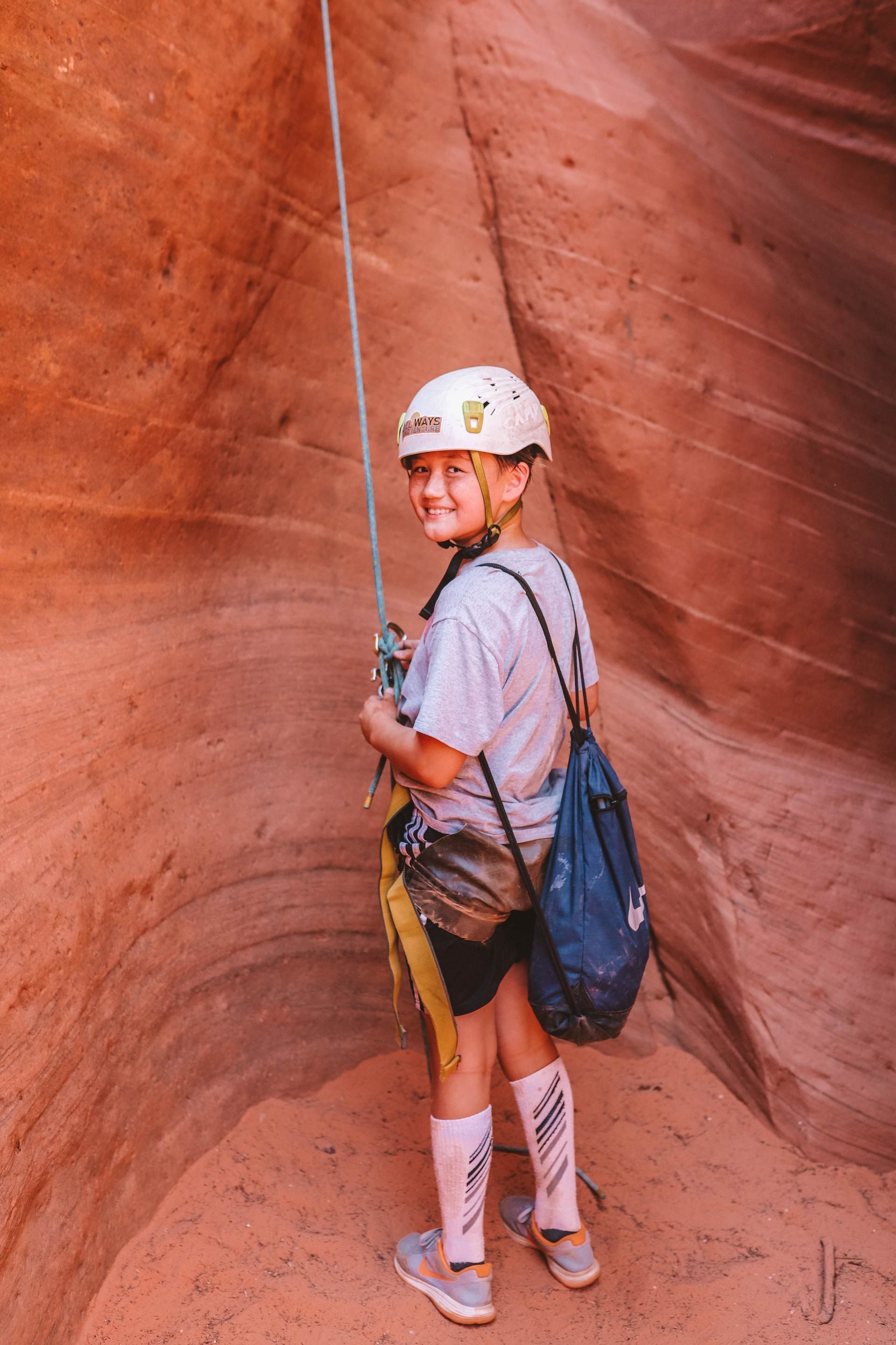 Rappelling in a red rock canyon, wearing a helmet, harness, and pack