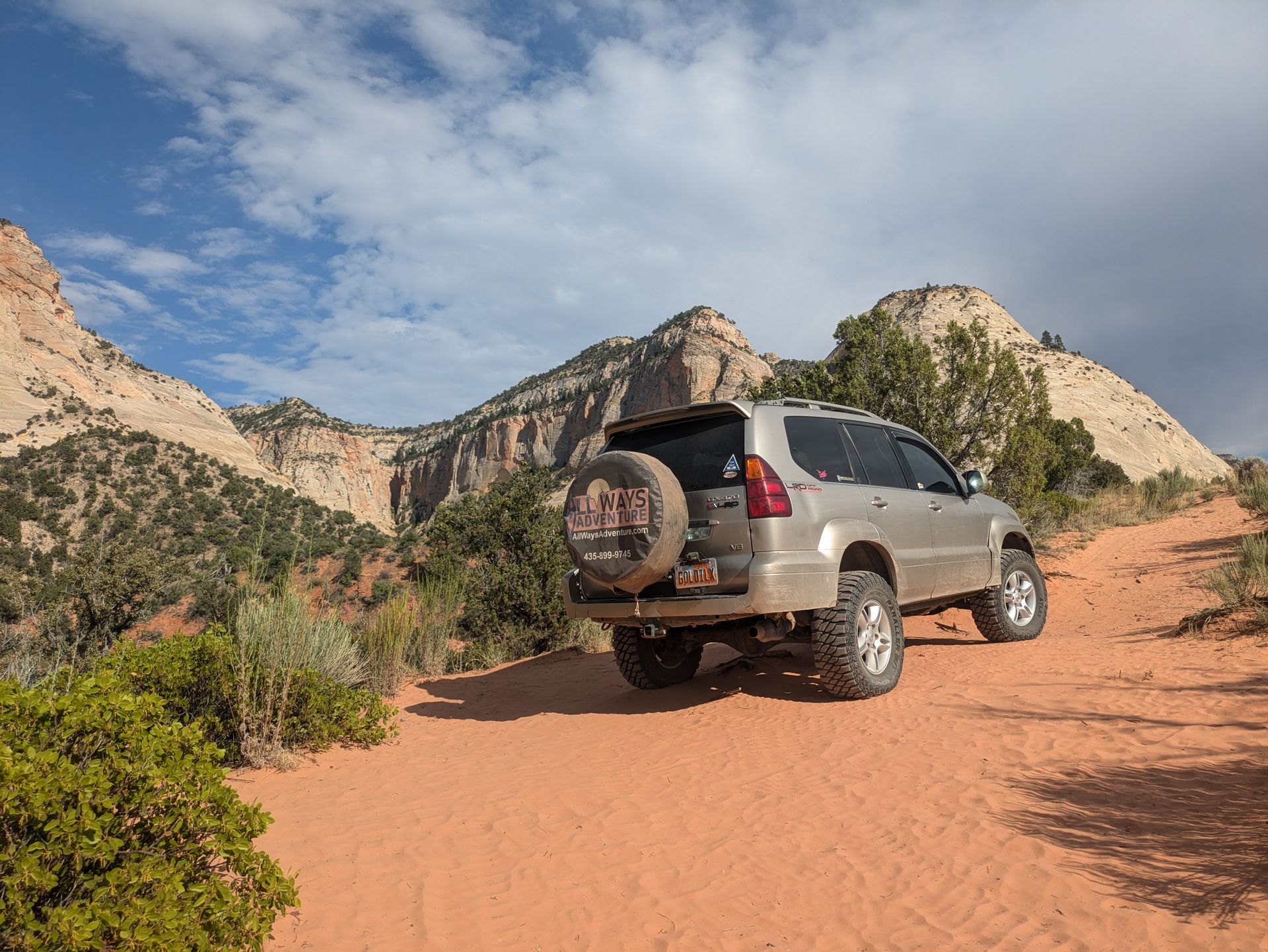 Tan SUV on a red dirt road with mountains in the background under a blue sky.