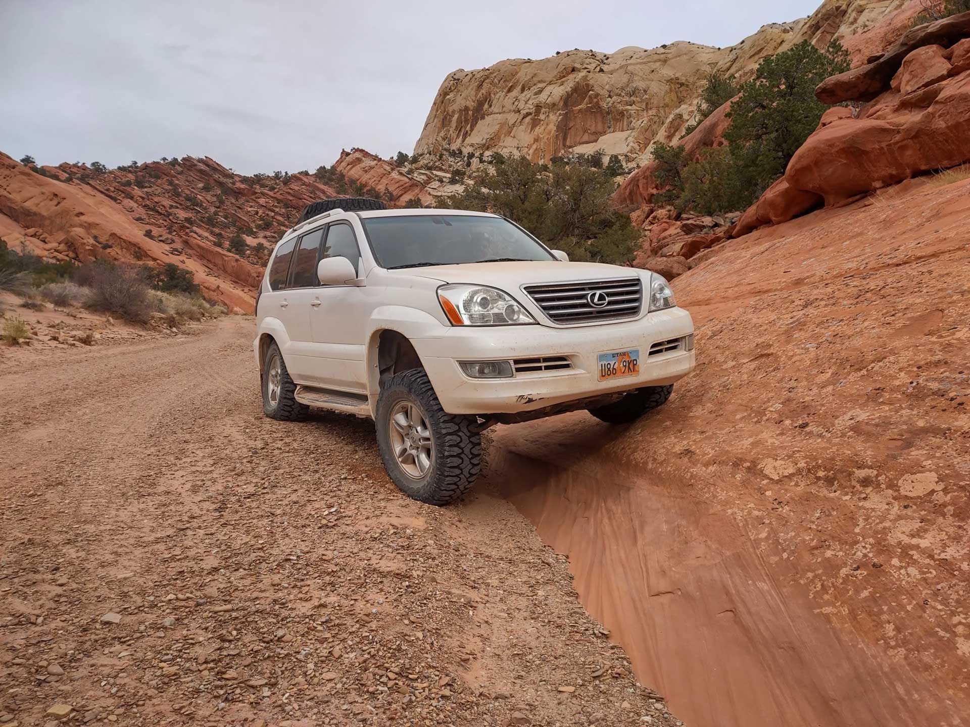 White SUV driving on a dirt road through a canyon, red rocks in background.