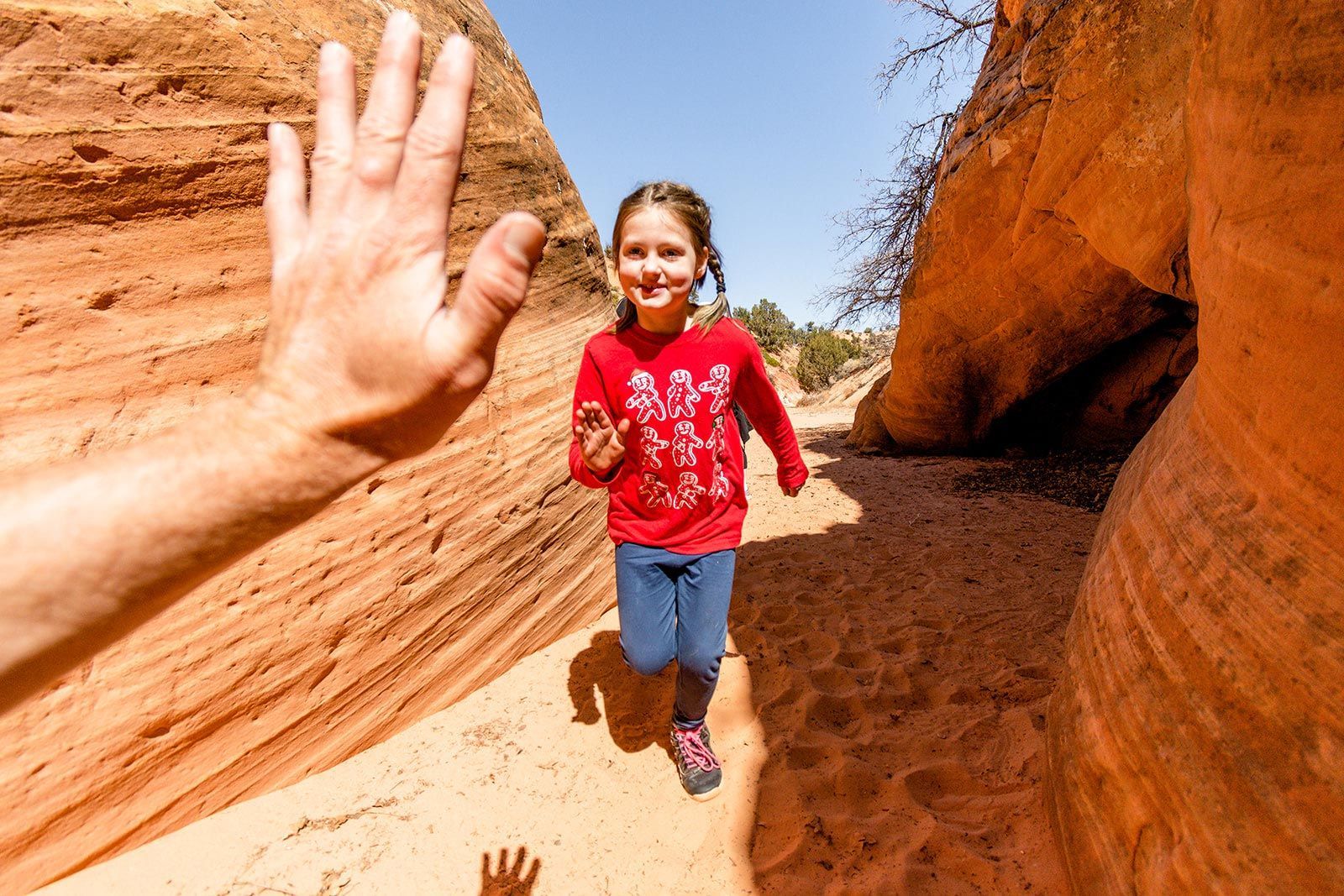 A smiling girl runs towards the camera, reaching for a high five, in a red-rock canyon.