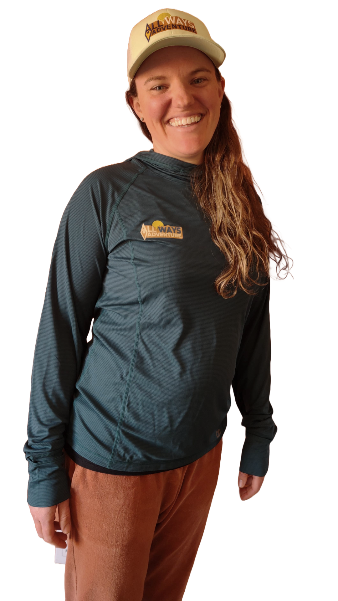 Woman wearing a hat and long-sleeved shirt, smiling, with brown pants.