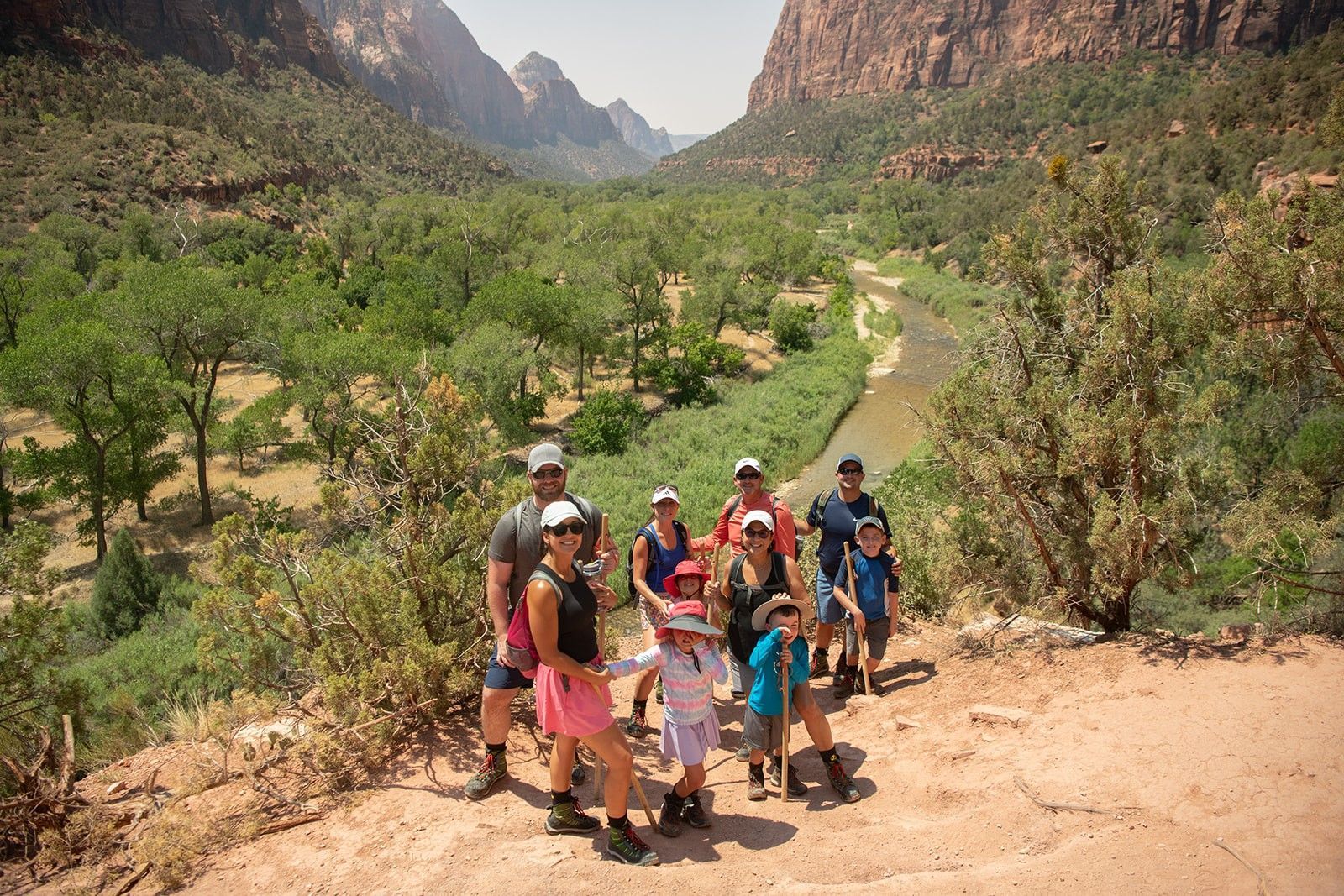 Group of people standing on a dirt path overlooking a canyon with a river below, Zion National Park.