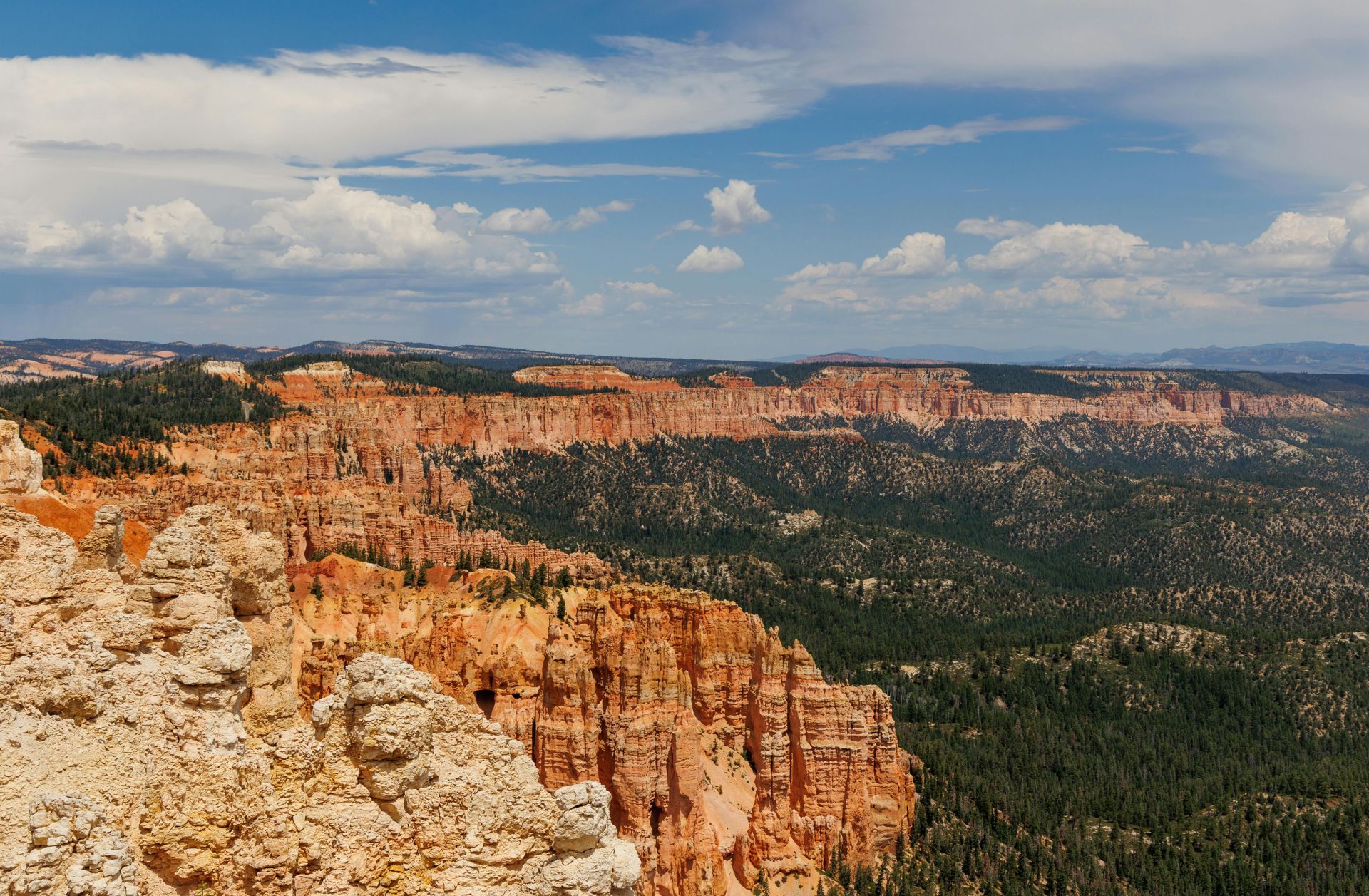 Scenic view of Bryce Canyon National Park with red rock formations, green forests, and a blue sky with clouds.