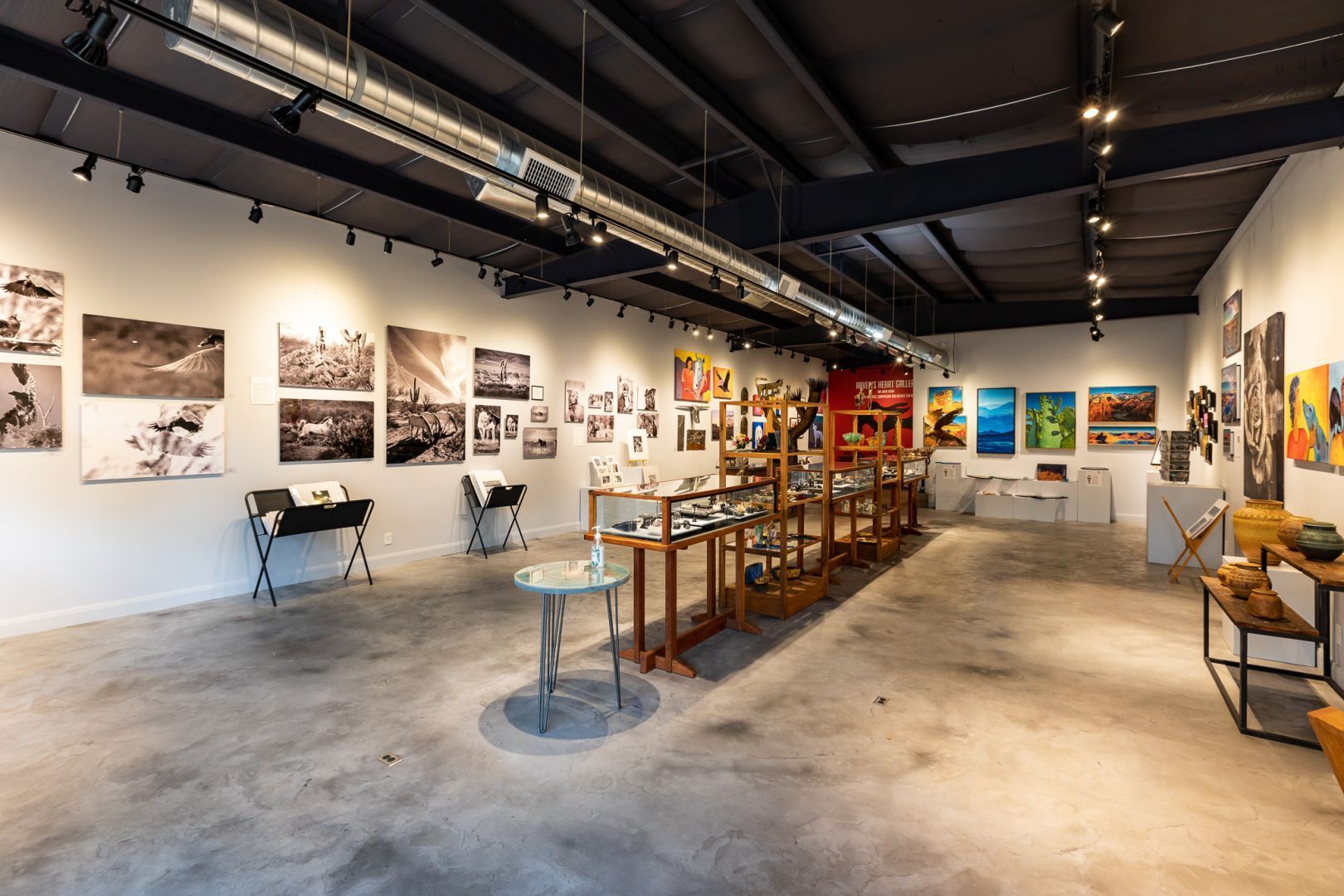 Interior of an art gallery with framed artwork on white walls, a variety of sculptures and objects on display.
