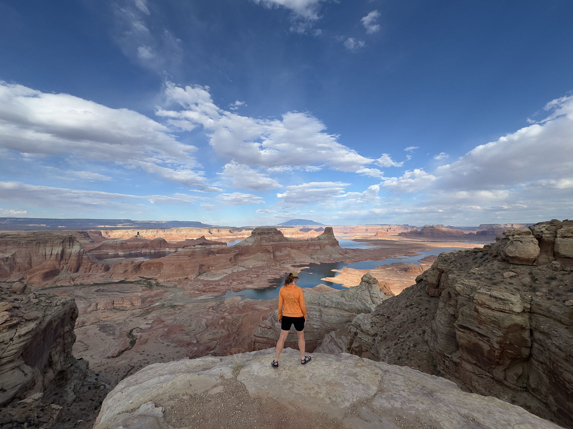 A woman is standing on top of a rocky cliff overlooking a lake.