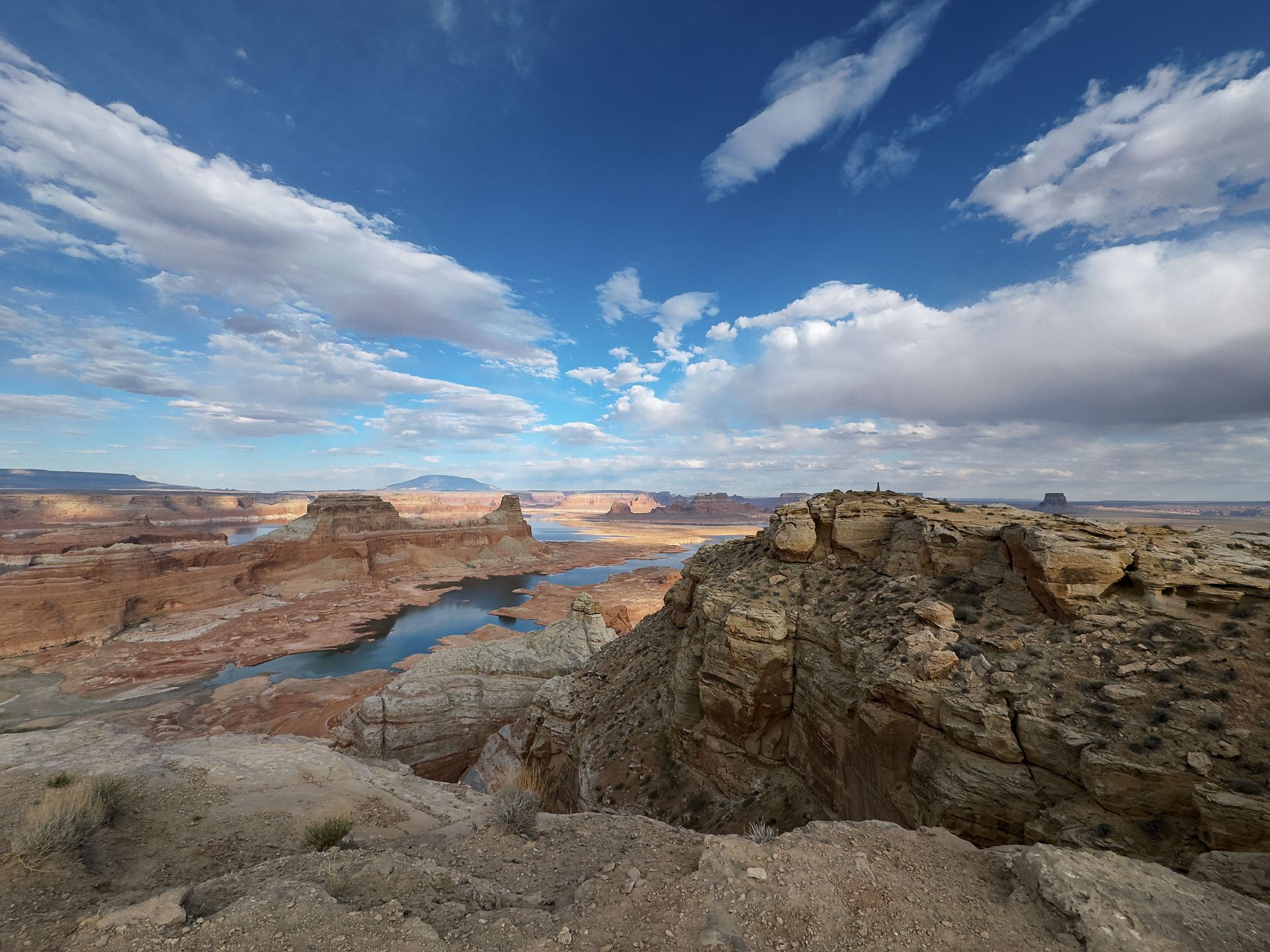 Overlook of a desert landscape with a blue lake winding through canyons. Bright blue sky with white clouds.