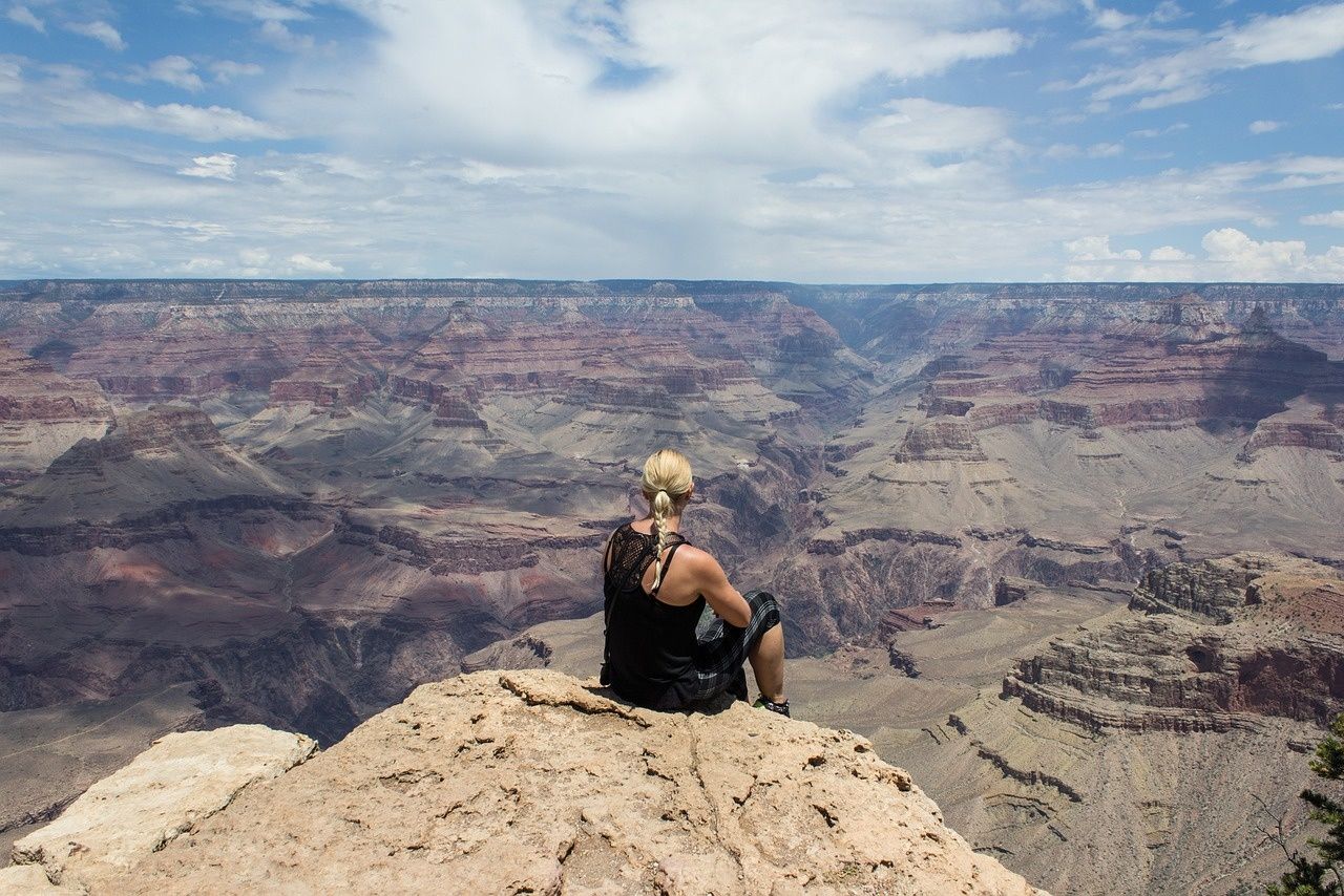 A woman is sitting on top of a rock overlooking a canyon.