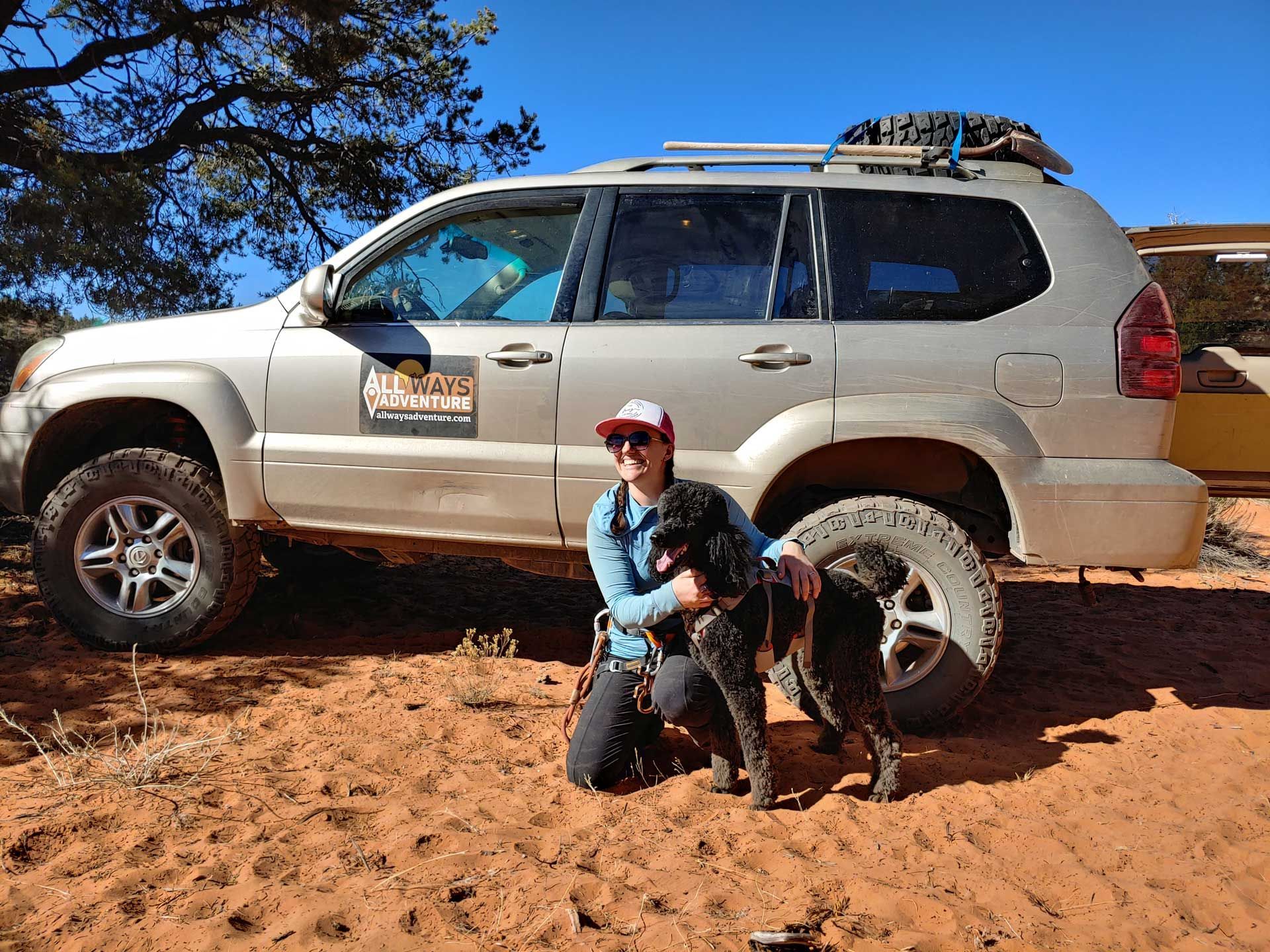 A man and a dog are kneeling in front of a suv.