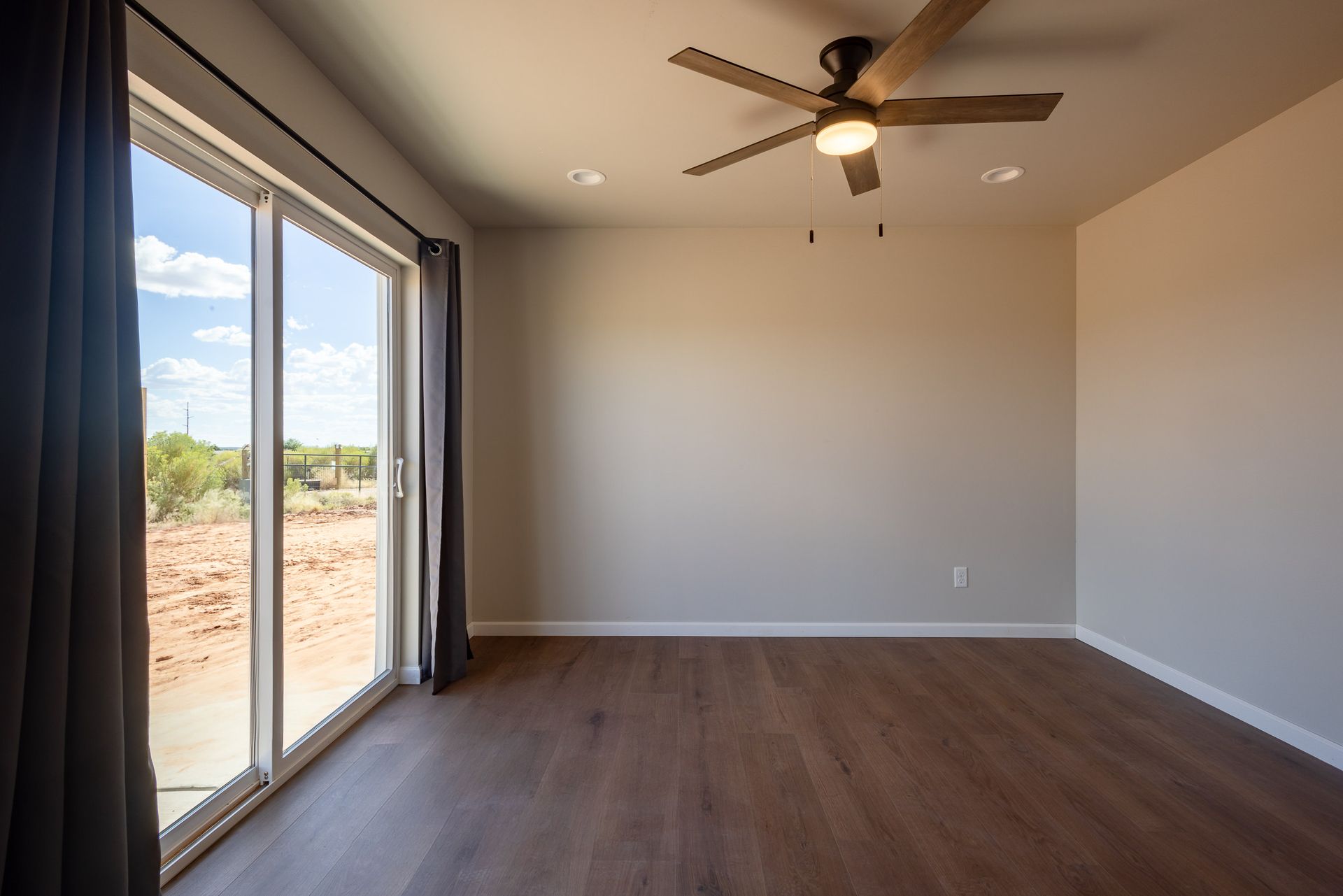 Empty room with sliding glass doors, ceiling fan, and dark wood floors.