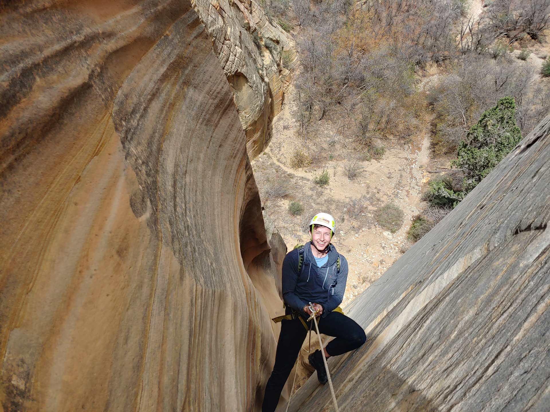 Man rappelling down a sandstone canyon, wearing a helmet and climbing gear.