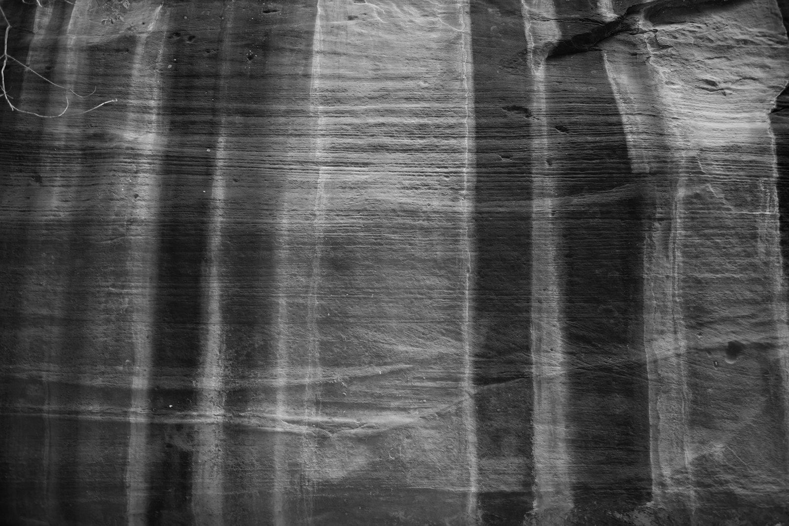 Black and white close-up of striated rock face with vertical streaks of light reflecting off a layered surface.