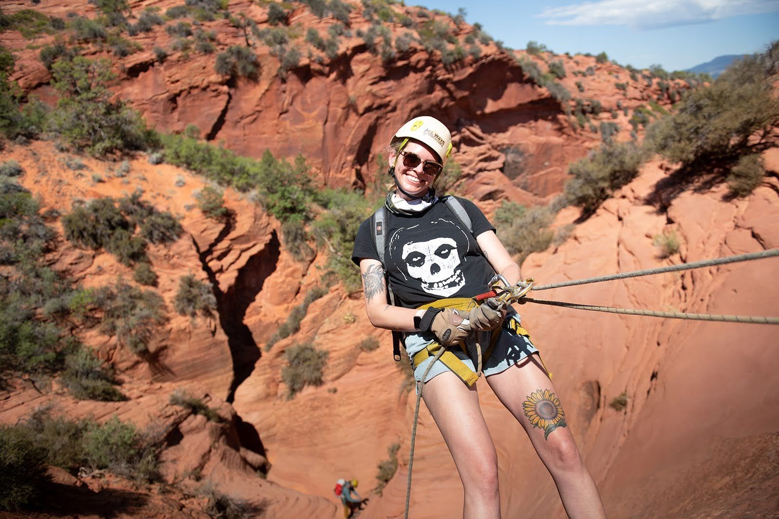 A woman is standing on top of a cliff wearing a helmet and shorts.