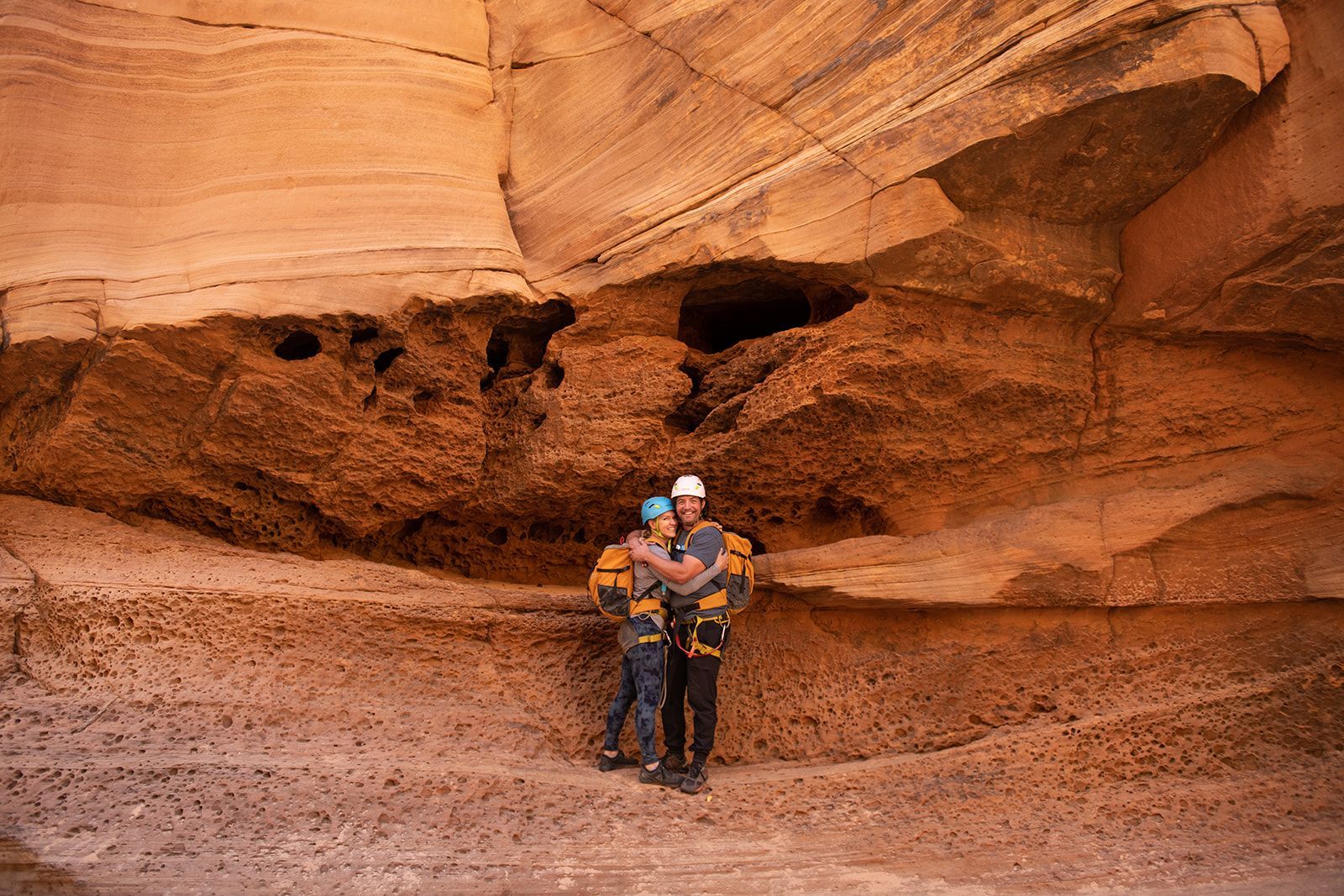 Three people hiking in red jackets through a red rock landscape under a blue sky.