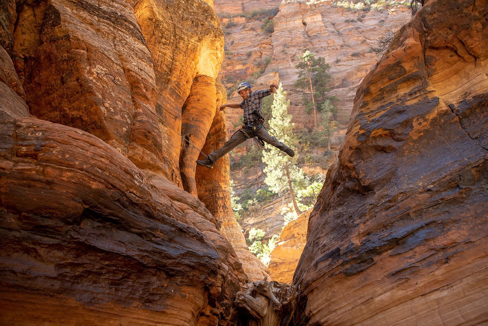 Person jumping in a narrow canyon. They're suspended mid-air. Red rock canyon walls, sunny day.