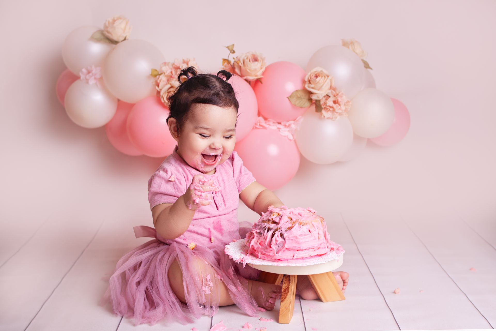 Una niña está sentada en el suelo comiendo un pastel rosa.