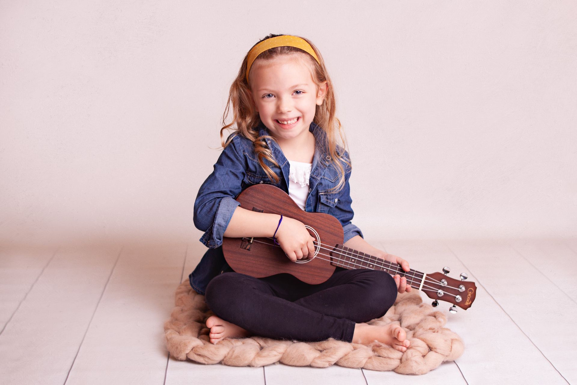 Una niña está sentada en el suelo sosteniendo una guitarra.