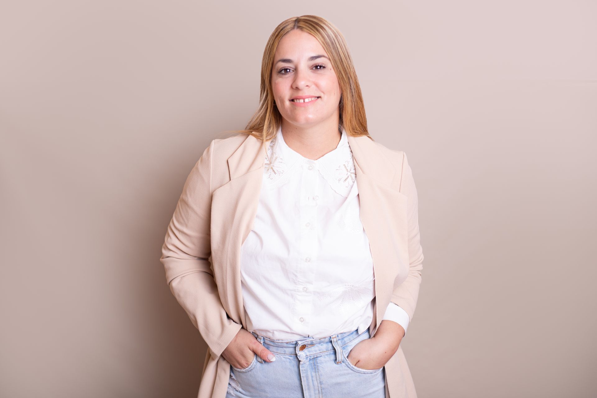 Una mujer está de pie con las manos en los bolsillos y sonriendo.