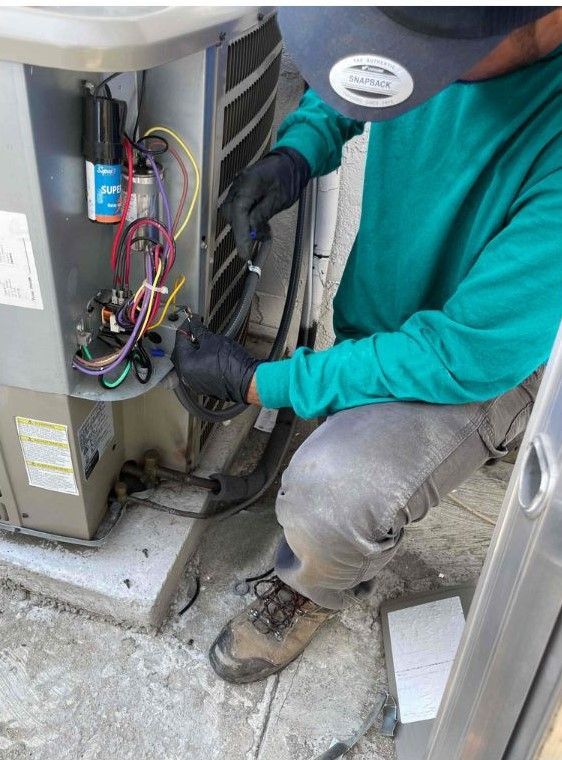 A man is kneeling down working on an air conditioner.