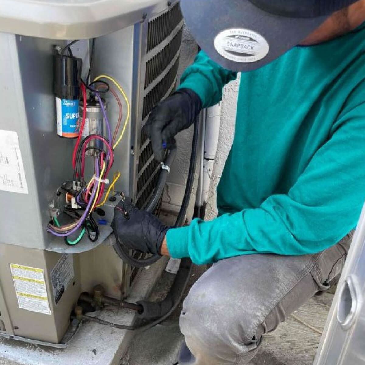 A man wearing a hat is working on an air conditioner.
