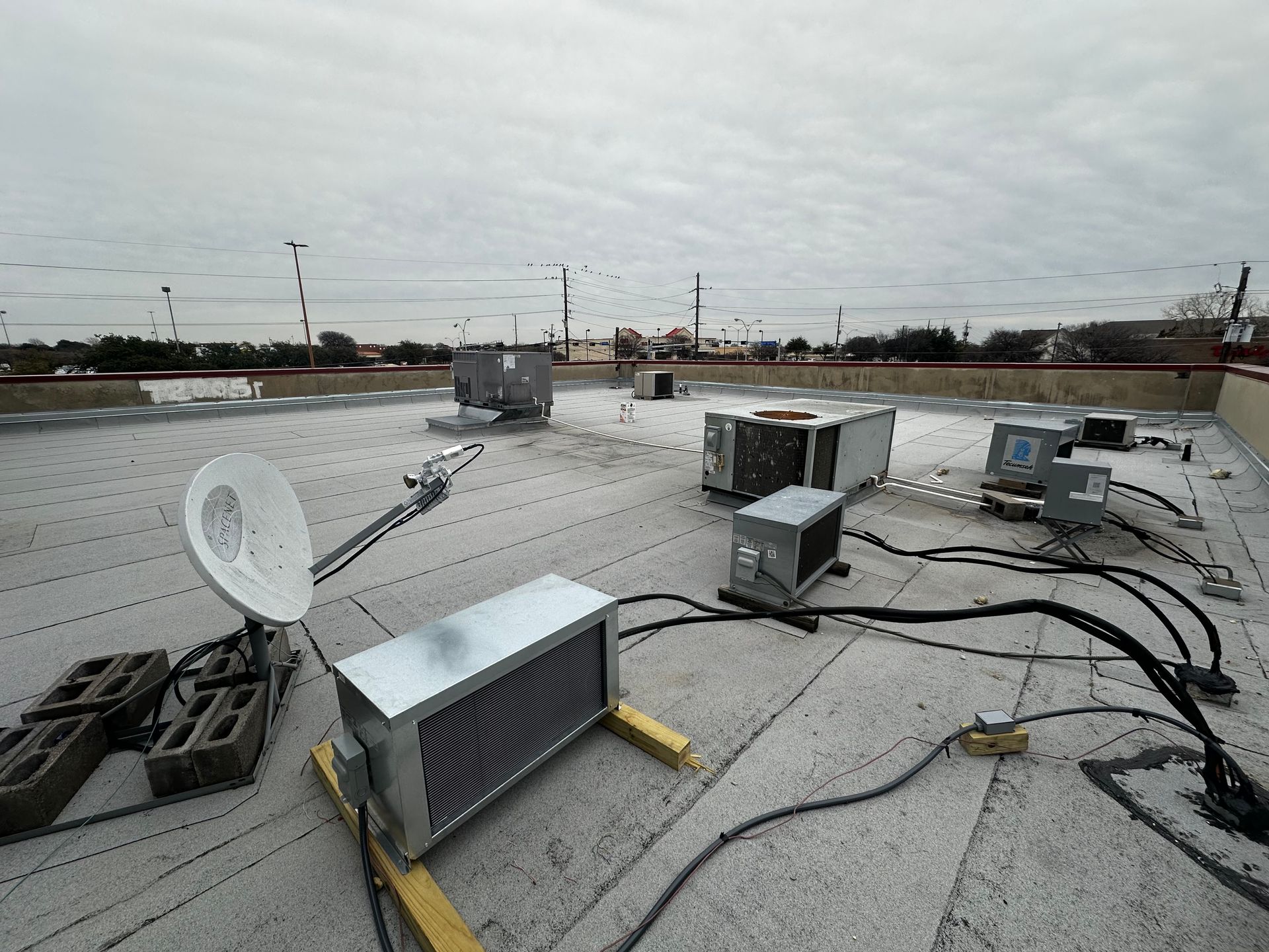 Rooftop with HVAC units, satellite dish, and electrical wiring under an overcast sky.
