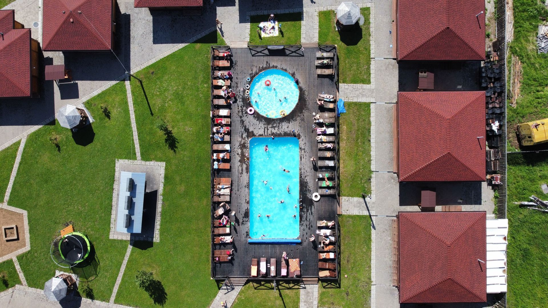Aerial view of a resort pool area with loungers, grass, and red-roofed buildings surrounding the pools.