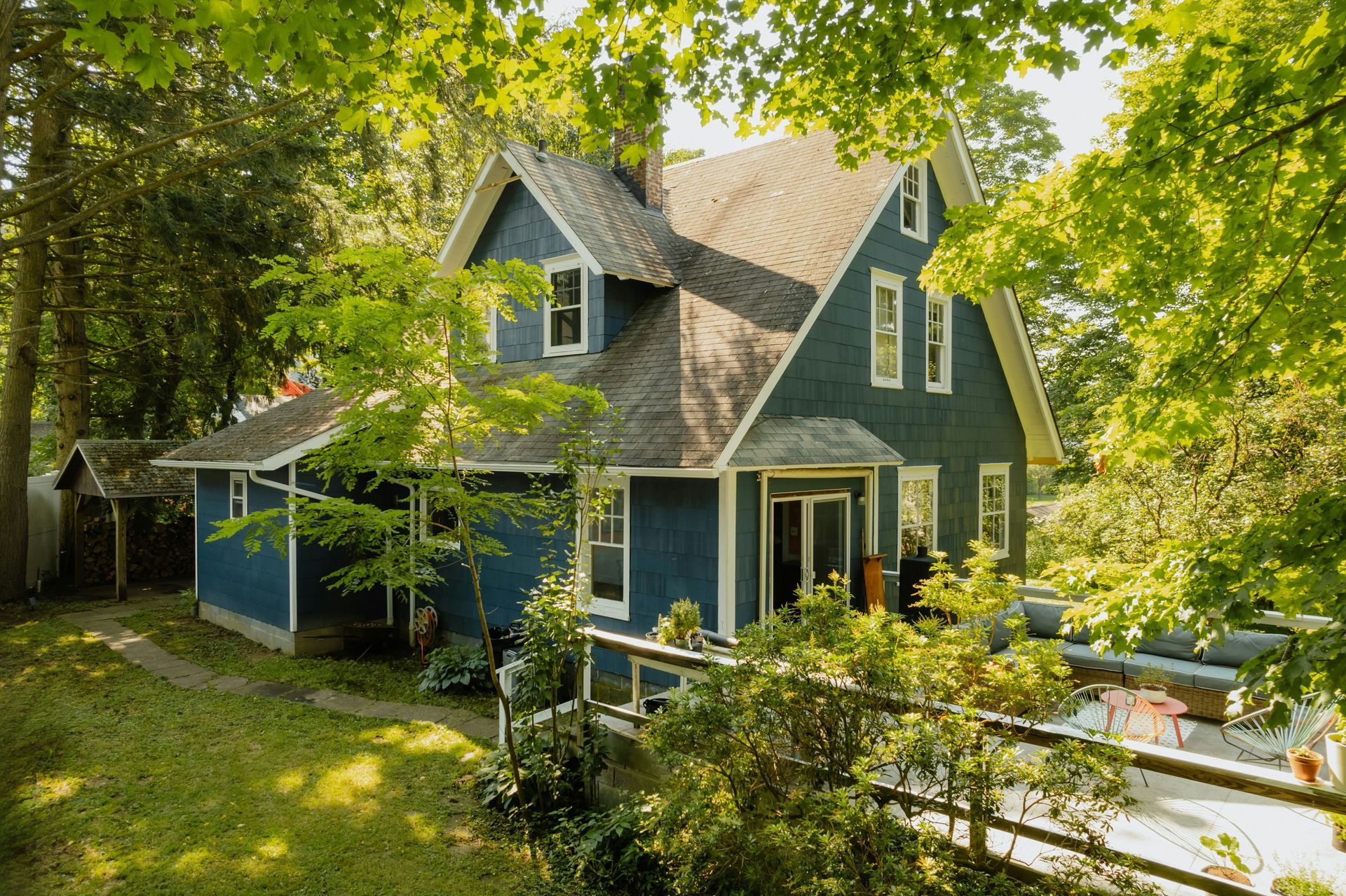 Blue house with a steep roof nestled in lush green trees and shrubs