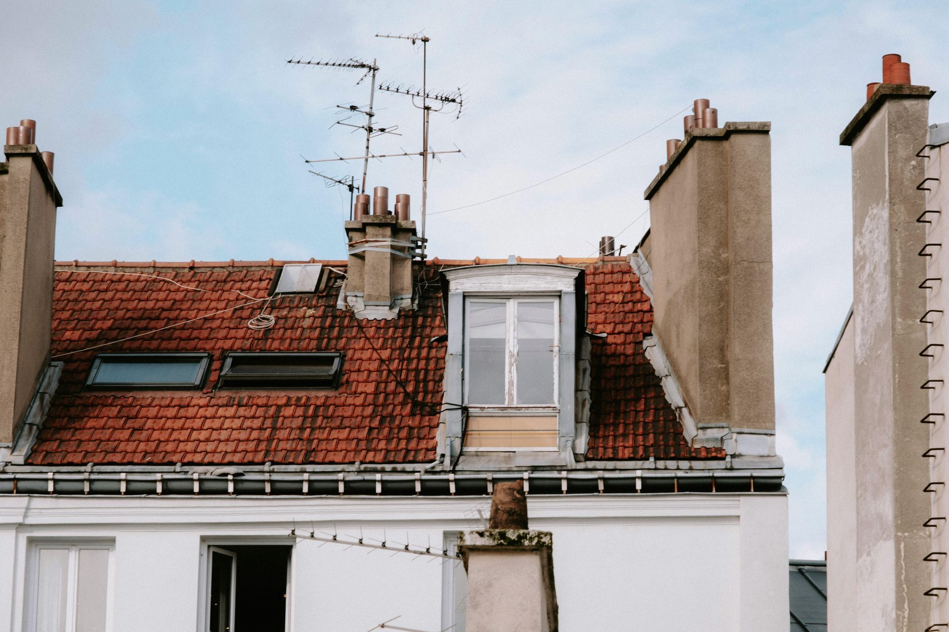 Rooftops with red tiles, chimneys, and TV antennas against a pale sky