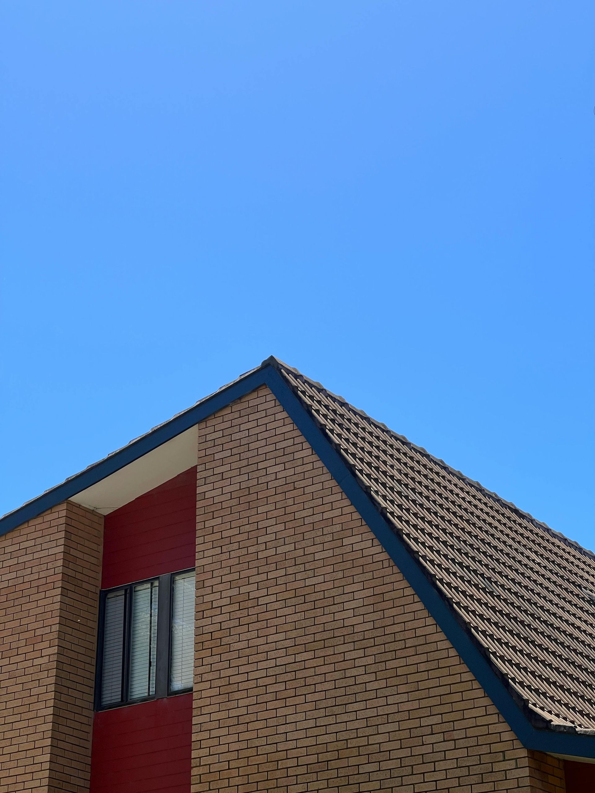 Corner of a brick building with a red facade and dark trim against a clear blue sky