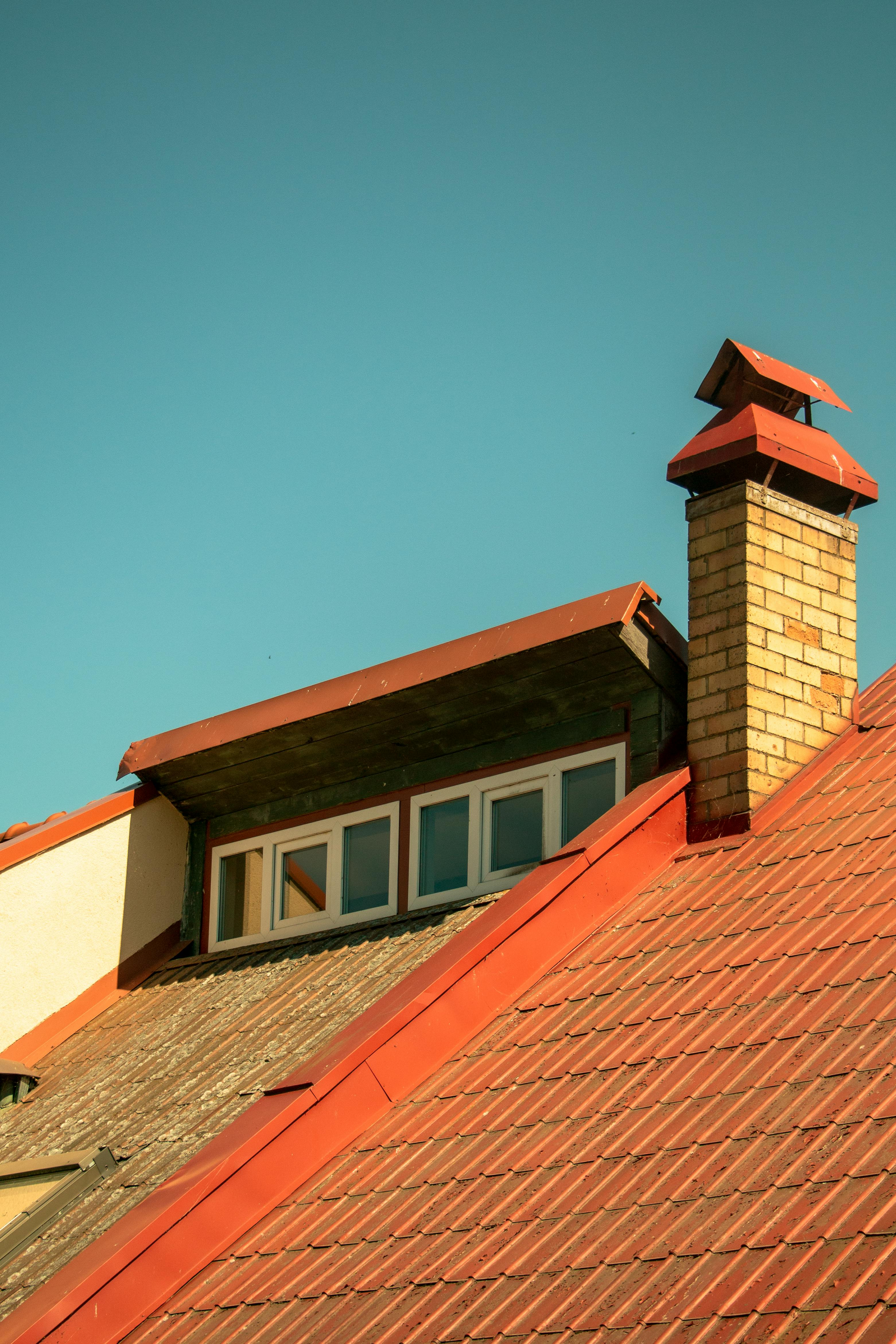 Red-tiled house roof with a brick chimney against a clear blue sky
