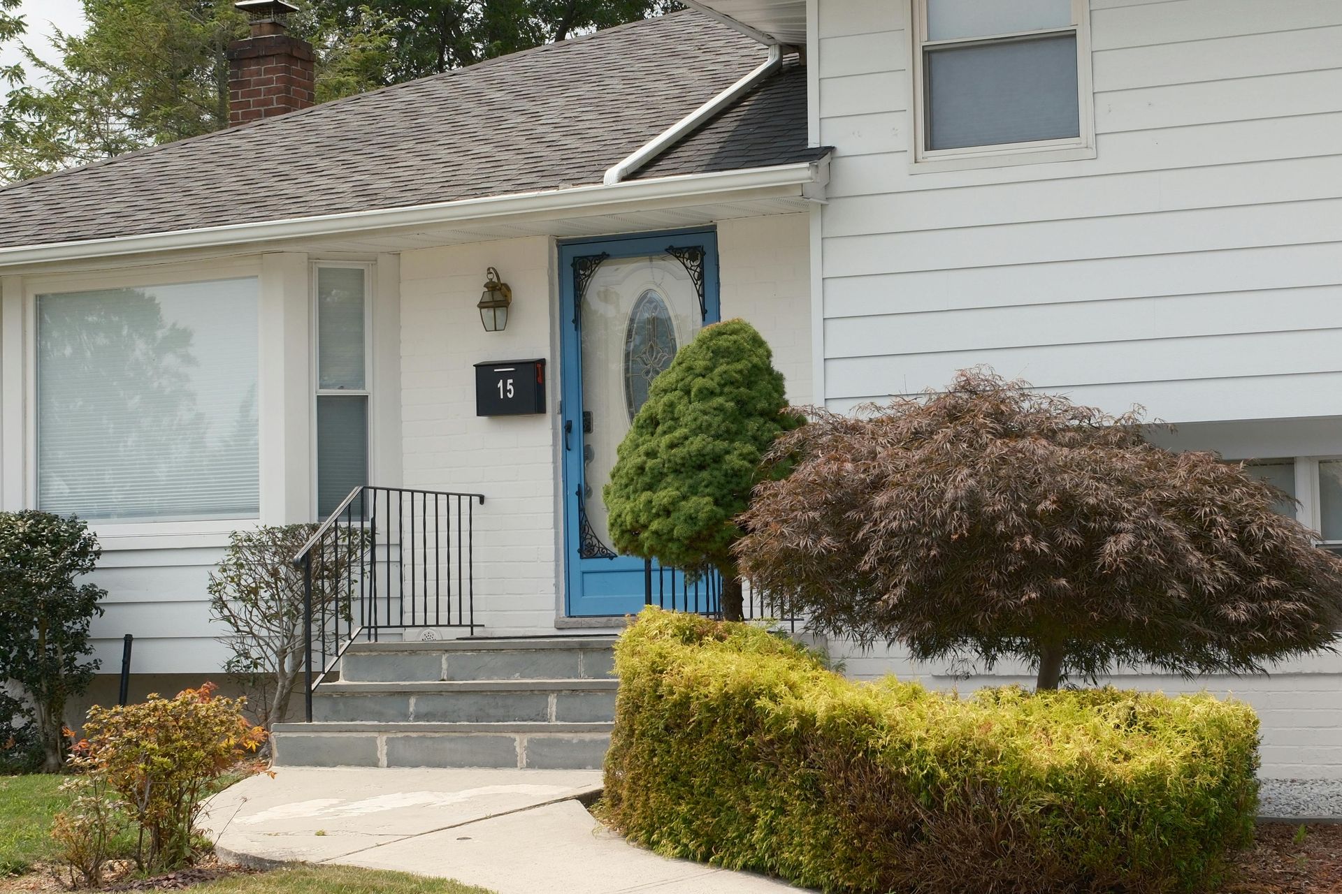 Suburban house entrance with blue front door, white siding, small porch, and trimmed shrubs