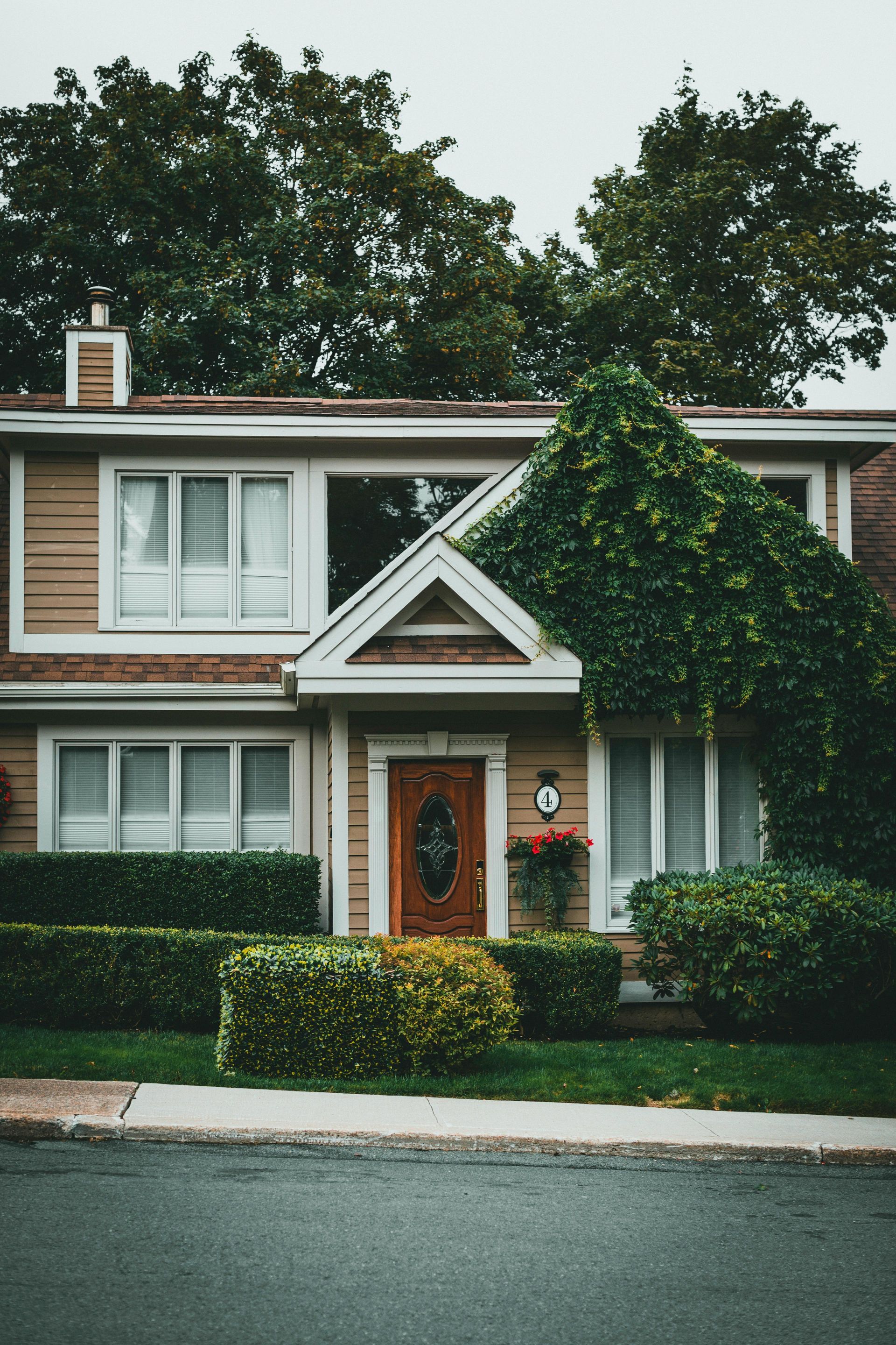 Two-story suburban house with brown siding, white trim, ivy-covered front entry, and trimmed hedges.