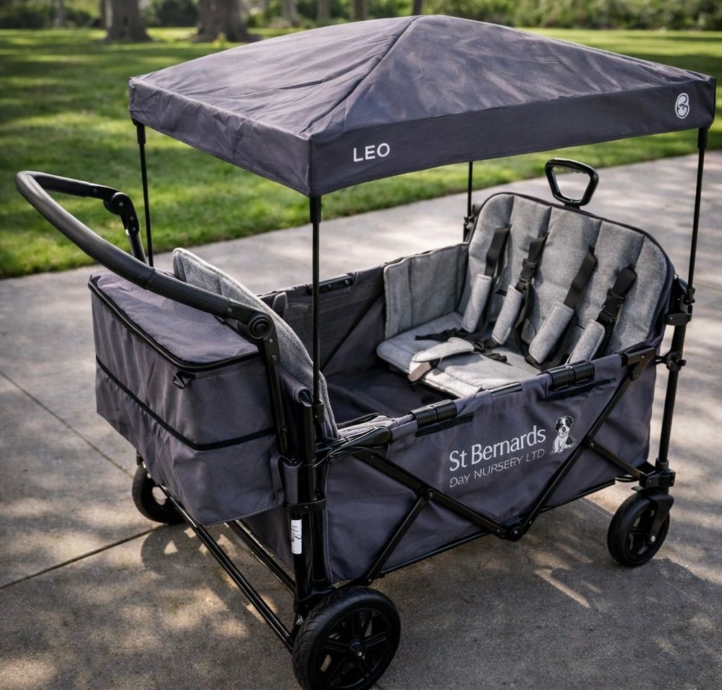 Gray wagon stroller with canopy and seat cushions parked on a sidewalk near grass