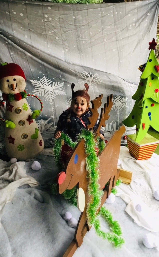 Child posing in a snowy holiday scene with a snowman, Christmas tree, and festive decorations