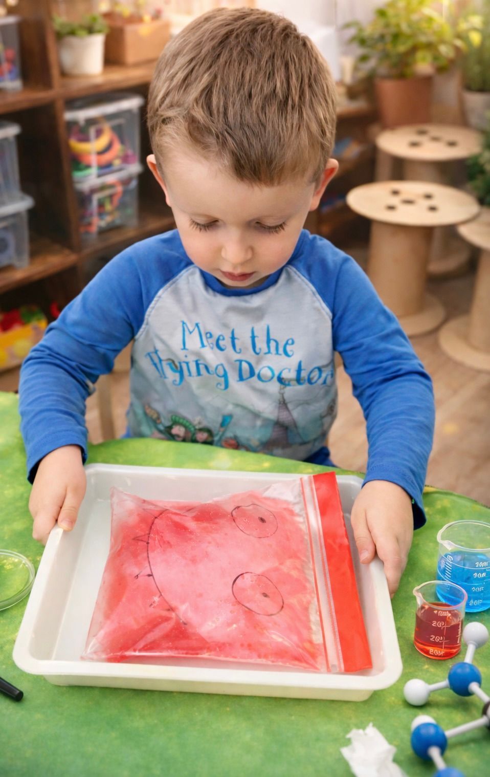 Child painting with red watercolor at a table in a classroom.