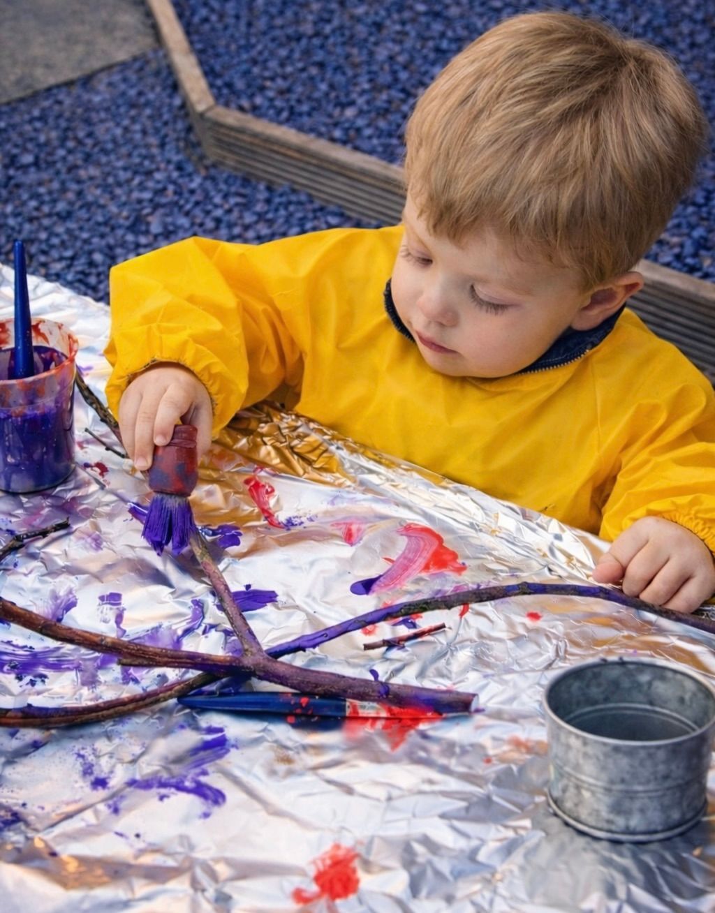 Child painting with purple paint on foil-covered table in an art activity.