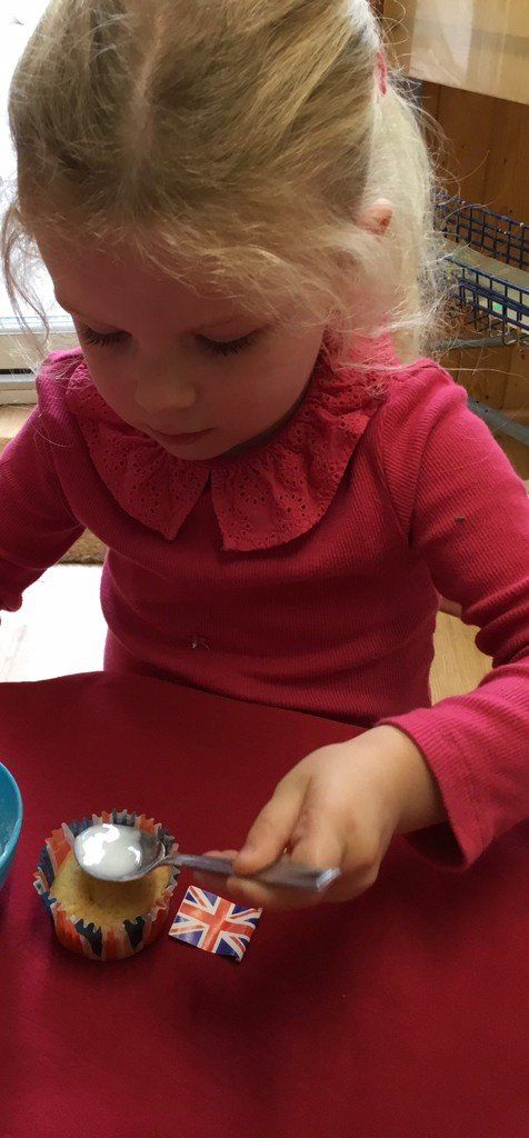 Child in a red top playing with a small Union Jack toy and a round ornament on a table.