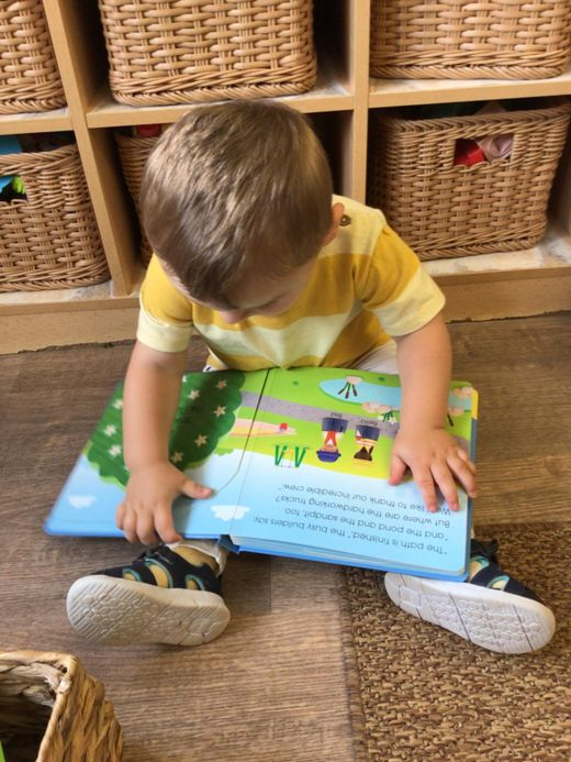 Child sitting on a rug, reading a colorful book in a cozy room with wicker baskets.