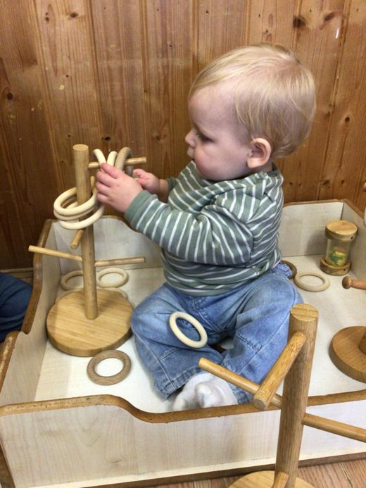 Toddler in striped shirt playing with wooden toys in a play area