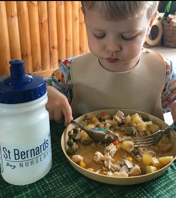 Child eating from a bowl at a table, with a St. Bernard's Day Nursery water bottle beside them