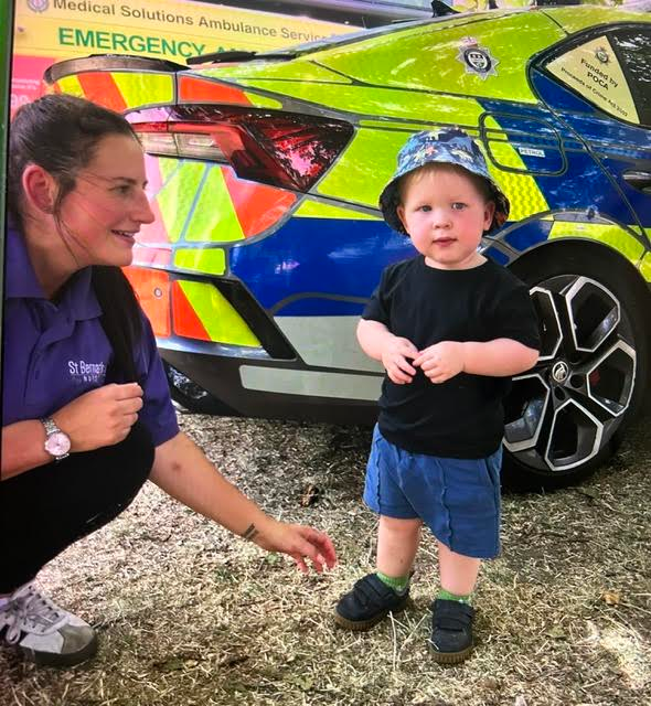 Woman crouches beside toddler in front of a colorful ambulance