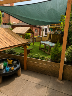 Backyard patio with wooden playhouse, green shade sail, and picnic table on a grassy lawn