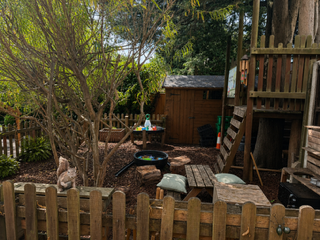Backyard patio with wooden deck, picnic table, tree, and playset behind a fence