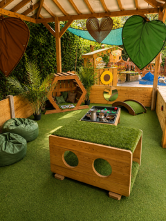 Cozy wooden play area with green turf, beanbags, and leaf decorations under a canopy