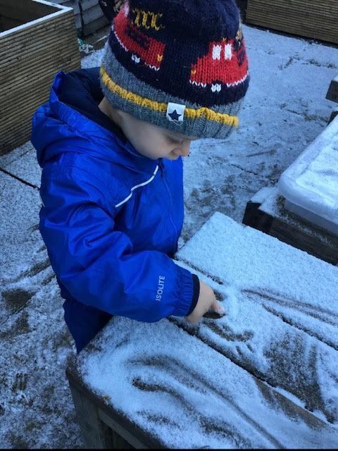 Child in blue jacket and knit hat playing in snow on a frosty bench.