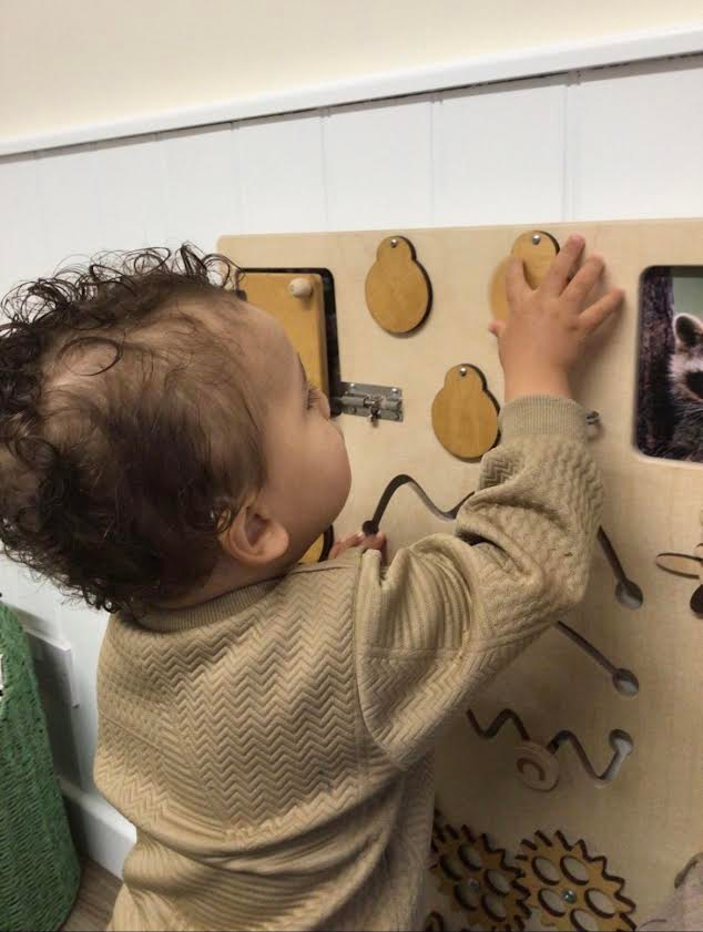 Child reaching for a wooden wall puzzle in a play area